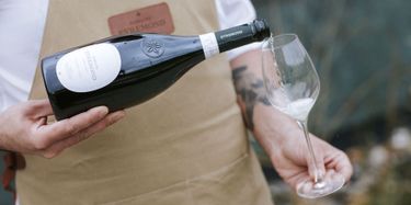 A close-up view of a person pouring Domaine Evremond English quality sparkling wine into a branded wine glass. The image highlights the careful craftsmanship and elegance associated with Domaine Evremond wines. The setting suggests a refined tasting experience celebrating premium sparkling wine.