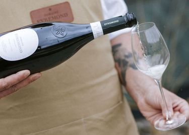 A close-up view of a person pouring Domaine Evremond English quality sparkling wine into a branded wine glass. The image highlights the careful craftsmanship and elegance associated with Domaine Evremond wines. The setting suggests a refined tasting experience celebrating premium sparkling wine.