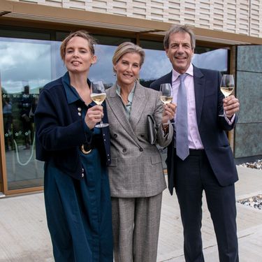 Three elegantly dressed guests hold glasses of sparkling wine outside the Domaine Evremond estate building. This scene highlights a refined tasting or celebratory moment associated with English quality sparkling wine. The modern architectural setting reflects premium craftsmanship and the estate's dedication to excellence.