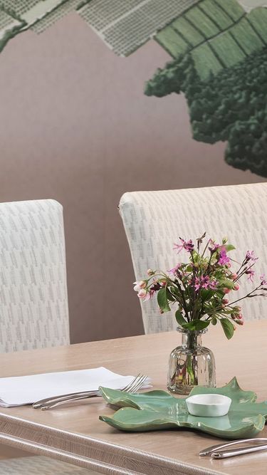 A refined meeting room featuring a long wooden table with four upholstered white chairs. The table is decorated with a small vase of fresh flowers, glassware, and neatly arranged cutlery. A large wall map providing a subtle backdrop enhances the sophisticated, professional atmosphere.