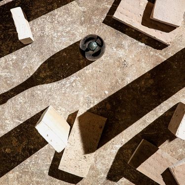 A composition of scattered light-colored bricks and a dark spherical object cast strong shadows on a textured surface. The image emphasizes the contrast between light and shadow, with an abstract, geometric arrangement. No direct connection to wine or vineyard settings is visible.