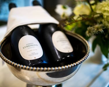 Two bottles of Domaine Evremond Classic Cuvée English quality sparkling wine displayed in an elegant silver ice bucket with a white napkin. The premium craftsmanship of the sparkling wine is highlighted by the refined presentation. This image reflects the sophistication associated with Domaine Evremond, a producer based in Chilham, Kent.