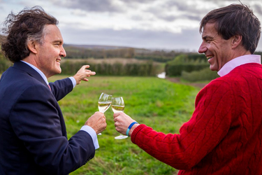 Two men enjoy a tasting of Domaine Evremond English quality sparkling wine in a lush vineyard setting. The scene captures the premium craftsmanship and scenic beauty of the estate in Chilham Kent. The moment highlights conviviality and appreciation for fine sparkling wine amidst rolling green hills.