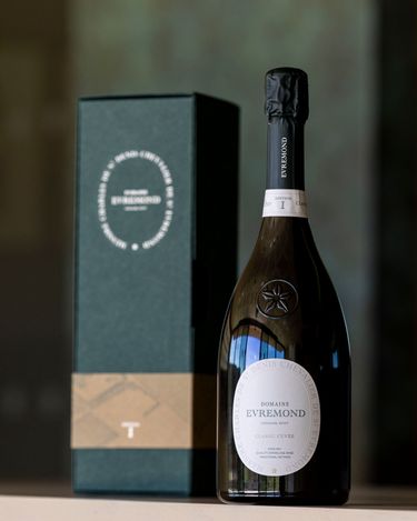 A bottle of Domaine Evremond Classic Cuvée English quality sparkling wine is presented alongside its elegant packaging. The label clearly identifies the wine as a premium sparkling wine from Chilham, Kent, showcasing traditional craftsmanship. The setting emphasizes the refined presentation suitable for a quality sparkling wine estate.