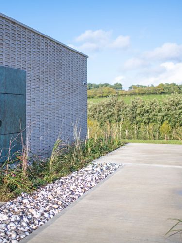 Modern exterior of Domaine Evremond winery set against vineyard landscapes in Kent. The image showcases the winery's contemporary architecture and the surrounding greenery of vineyard rows. This setting reflects the premium craftsmanship associated with English quality sparkling wine production.